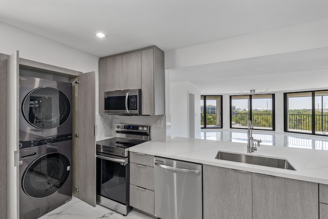 kitchen featuring stacked washer and dryer, marble finish floor, modern cabinets, a sink, and stainless steel appliances