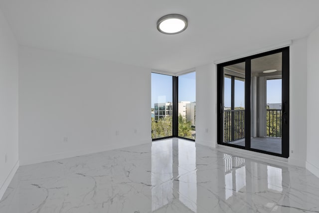 empty room featuring marble finish floor, a wall of windows, and baseboards