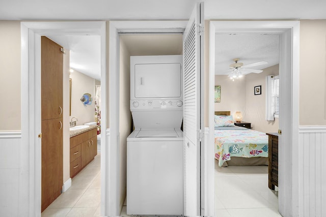 washroom with light tile patterned floors, stacked washer / drying machine, wainscoting, a sink, and laundry area