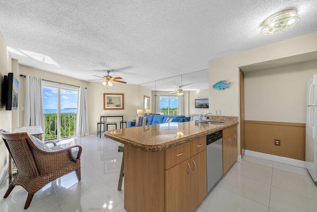 kitchen with a wainscoted wall, stainless steel dishwasher, light tile patterned flooring, a sink, and a peninsula