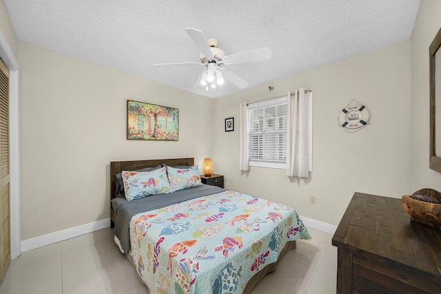 tiled bedroom with ceiling fan, a textured ceiling, and baseboards