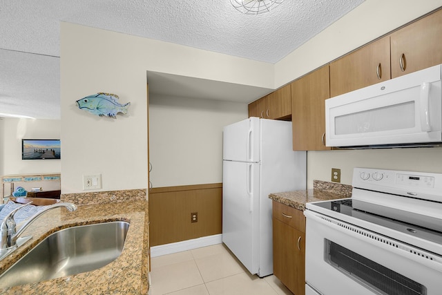 kitchen featuring white appliances, a wainscoted wall, a textured ceiling, a sink, and light tile patterned flooring