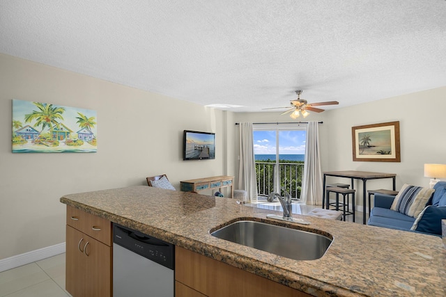 kitchen featuring a textured ceiling, dishwashing machine, a sink, baseboards, and open floor plan