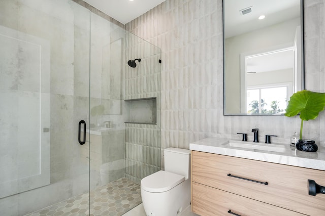 bathroom featuring toilet, a shower with shower door, tile walls, vanity, and backsplash