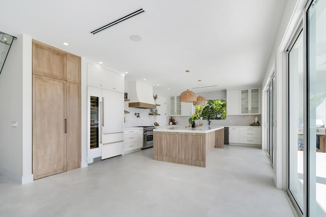 kitchen with decorative light fixtures, white cabinetry, premium appliances, a center island, and custom range hood