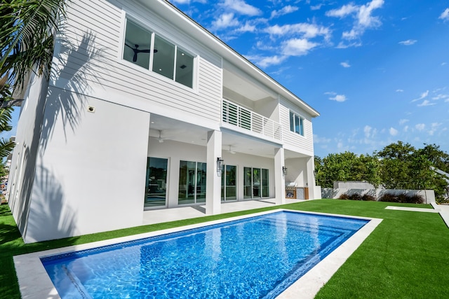 rear view of house with a fenced in pool, a lawn, a balcony, and ceiling fan