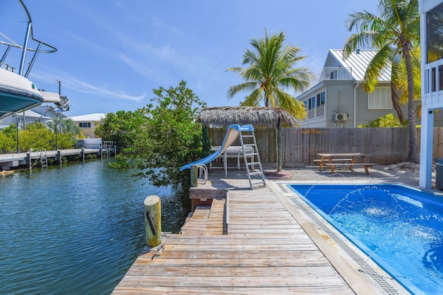 view of pool with a dock, fence, a fenced in pool, a water view, and a water slide