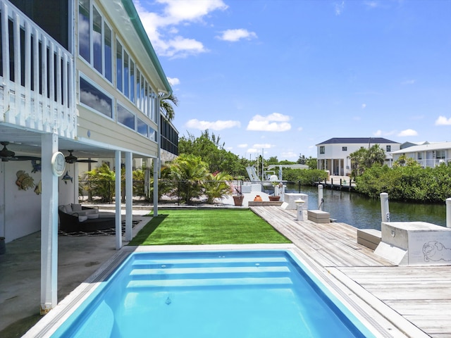 view of pool with ceiling fan, a boat dock, fence, a yard, and a water view