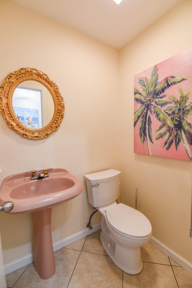 half bath featuring baseboards, a sink, tile patterned floors, and toilet