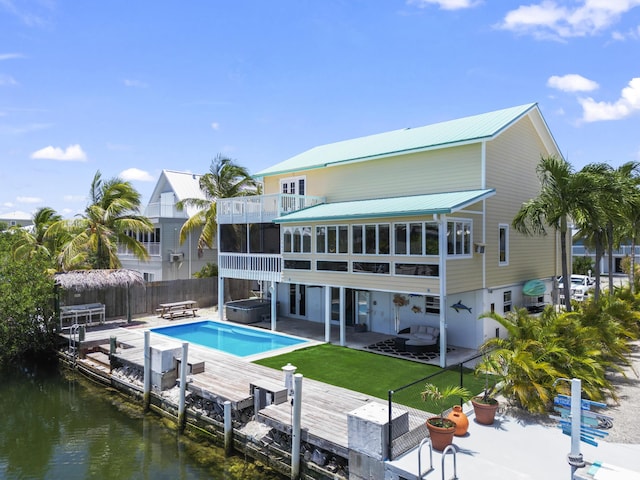 rear view of house featuring a water view, a sunroom, fence, a patio, and a jacuzzi