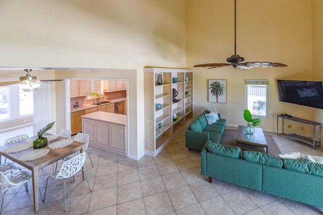 living room featuring baseboards, light tile patterned flooring, ceiling fan, and a high ceiling