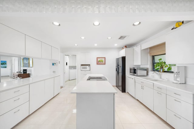 kitchen featuring sink, white appliances, a center island, white cabinets, and washer / dryer