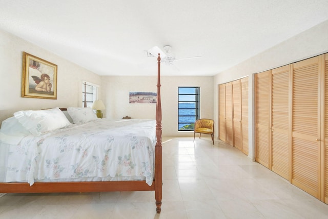 bedroom with ceiling fan, light tile patterned floors, and two closets