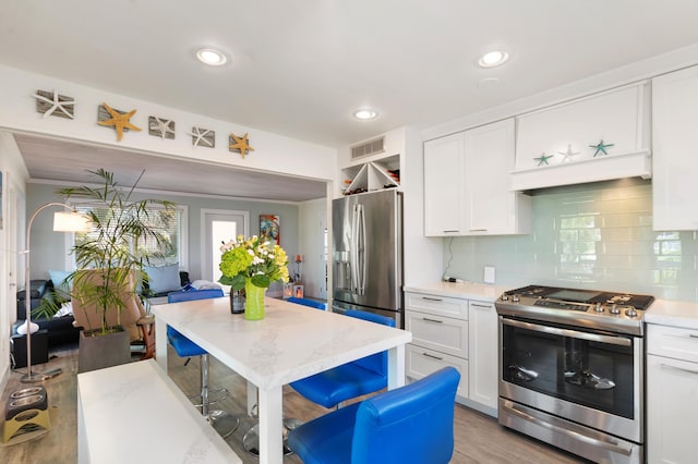 kitchen featuring white cabinetry, appliances with stainless steel finishes, light wood-type flooring, and backsplash