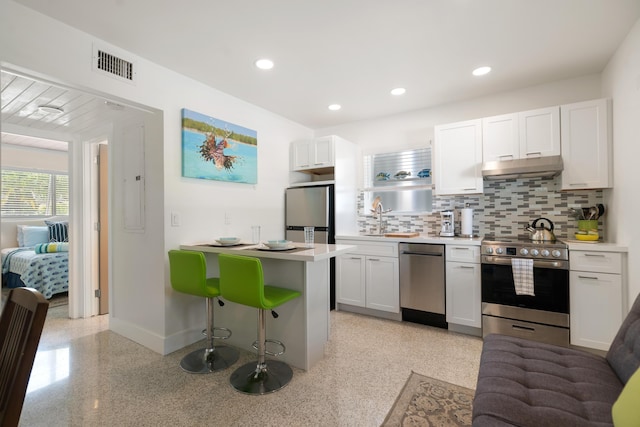 kitchen featuring sink, white cabinetry, stainless steel appliances, a kitchen bar, and decorative backsplash