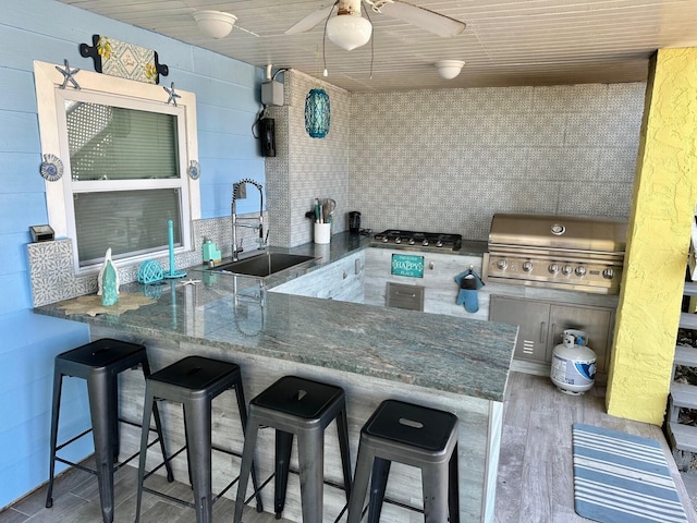 kitchen with a kitchen bar, sink, kitchen peninsula, ceiling fan, and hardwood / wood-style floors