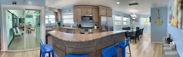 kitchen with a kitchen island, appliances with stainless steel finishes, a chandelier, a kitchen bar, and light hardwood / wood-style flooring