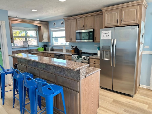 kitchen with a kitchen island, appliances with stainless steel finishes, stone countertops, a kitchen breakfast bar, and light wood-type flooring