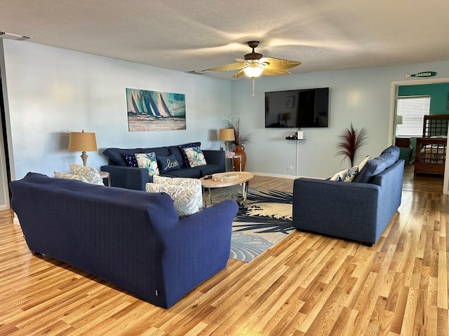 living room featuring ceiling fan, light hardwood / wood-style flooring, and a textured ceiling