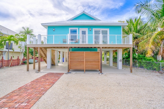 coastal inspired home featuring covered porch, fence, driveway, stairway, and a carport