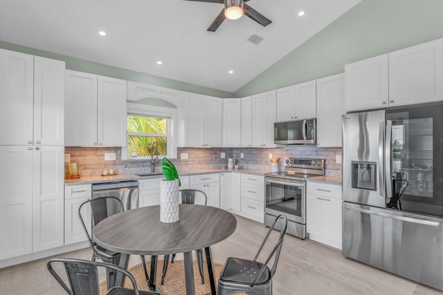 kitchen with white cabinets, a sink, vaulted ceiling, stainless steel appliances, and backsplash