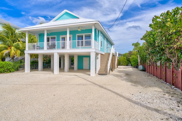 coastal inspired home with metal roof, a porch, dirt driveway, stairway, and a carport