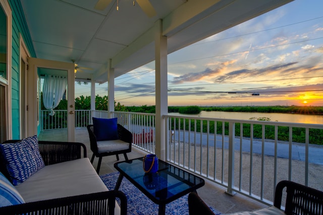 balcony at dusk featuring a ceiling fan and a water view