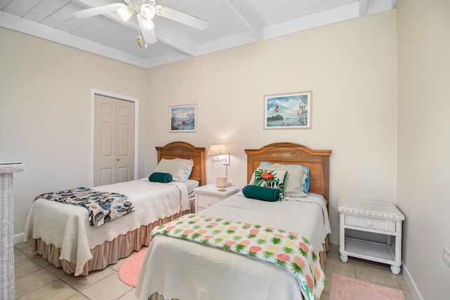 bedroom featuring ceiling fan, light tile patterned floors, beam ceiling, and a closet