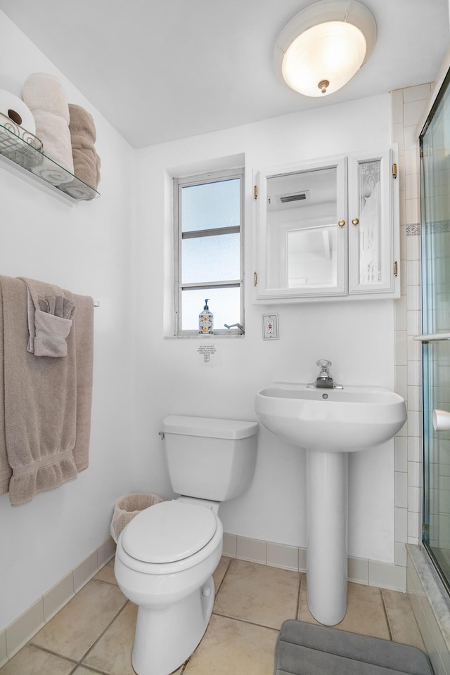 bathroom featuring a shower with door, tile patterned floors, and toilet