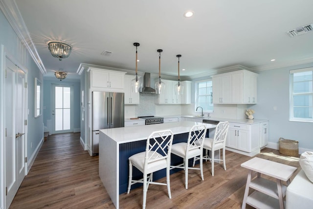 kitchen featuring visible vents, ornamental molding, appliances with stainless steel finishes, a sink, and wall chimney range hood