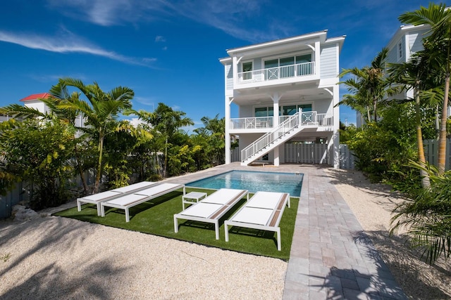 back of property featuring a balcony, fence, stairway, and an outdoor pool
