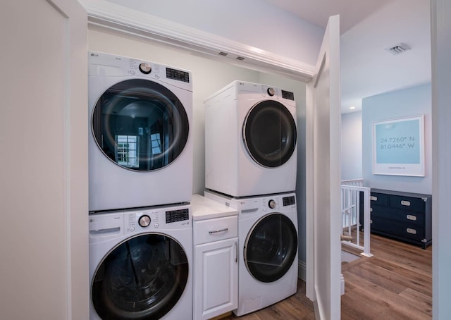 clothes washing area featuring stacked washer and dryer, cabinet space, light wood finished floors, and visible vents