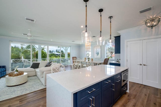 kitchen featuring stainless steel microwave, blue cabinetry, crown molding, and visible vents