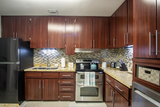 kitchen featuring tasteful backsplash, sink, double oven range, light stone countertops, and black fridge