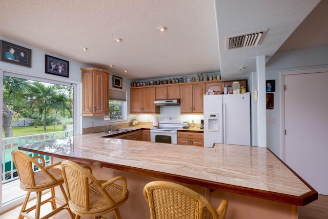 kitchen with sink, white appliances, a breakfast bar, a textured ceiling, and kitchen peninsula