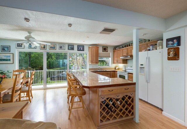 kitchen with sink, white appliances, light hardwood / wood-style flooring, a center island, and tile counters