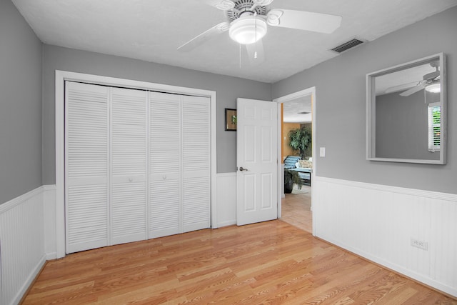 unfurnished bedroom featuring a wainscoted wall, visible vents, light wood-style flooring, ceiling fan, and a closet
