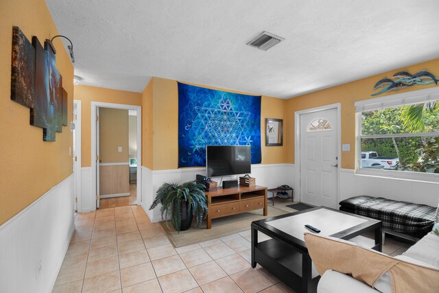 living area featuring light tile patterned floors, a wainscoted wall, a textured ceiling, and visible vents