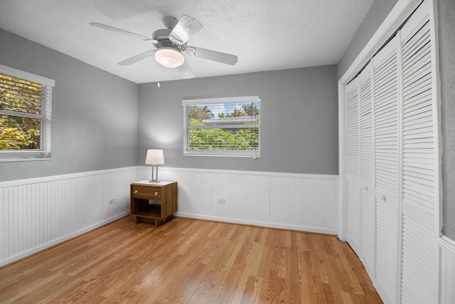 unfurnished bedroom featuring light wood-style flooring, multiple windows, a closet, and wainscoting
