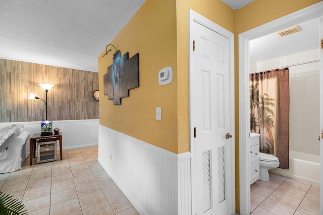 hall featuring a wainscoted wall, a textured ceiling, visible vents, and light tile patterned flooring