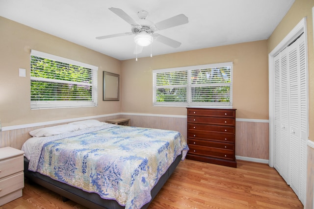 bedroom with wooden walls, ceiling fan, a wainscoted wall, wood finished floors, and a closet