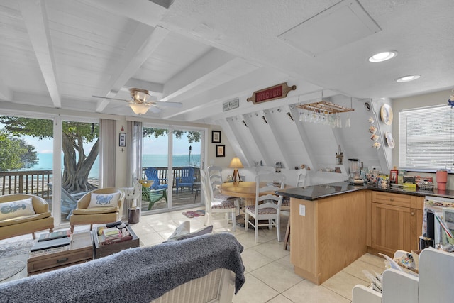 kitchen with beamed ceiling, light tile patterned floors, ceiling fan, kitchen peninsula, and a water view