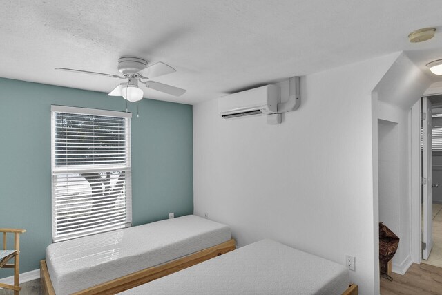 bedroom with ceiling fan, an AC wall unit, a textured ceiling, and light hardwood / wood-style floors