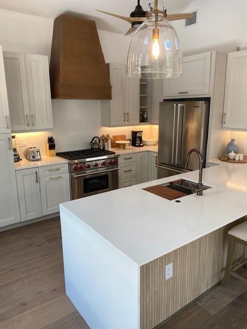 kitchen with high quality appliances, premium range hood, white cabinetry, and decorative light fixtures