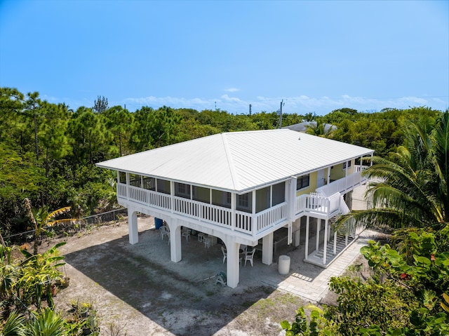 back of property with a forest view, stairway, metal roof, a sunroom, and driveway