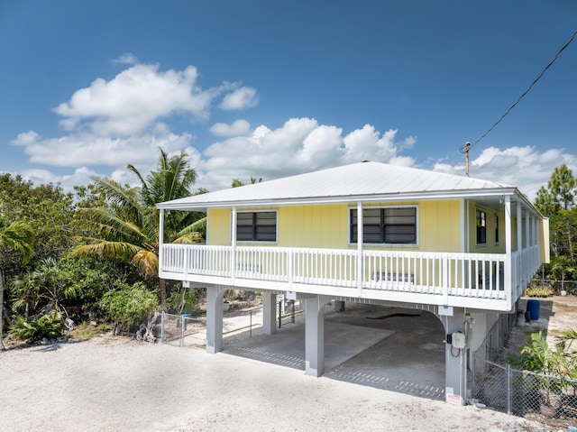 coastal inspired home with a carport, driveway, metal roof, and fence