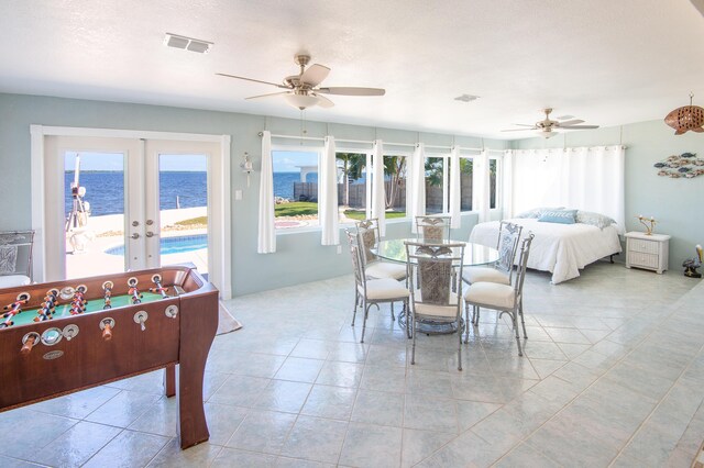 tiled dining room with a textured ceiling, french doors, ceiling fan, and a water view