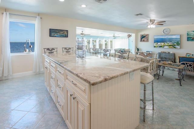 kitchen with a water view, a center island, a breakfast bar area, and light stone counters