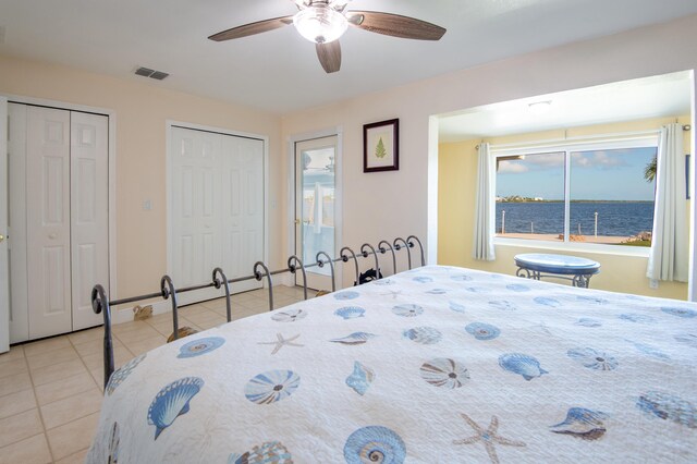 bedroom featuring a water view, ceiling fan, multiple closets, and light tile patterned flooring