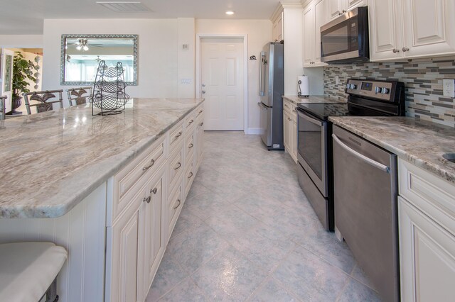 kitchen with appliances with stainless steel finishes, a breakfast bar, tasteful backsplash, white cabinets, and light stone counters